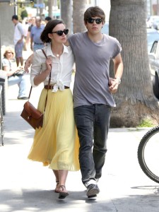 Keira Knightley wearing a yellow skirt, white shirt, and brown satchel